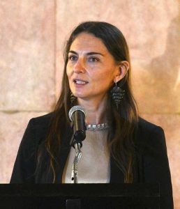 A headshot of Marina Núñez Bespalova, speaking at a microphone and wearing a light top and dark suit jacket.