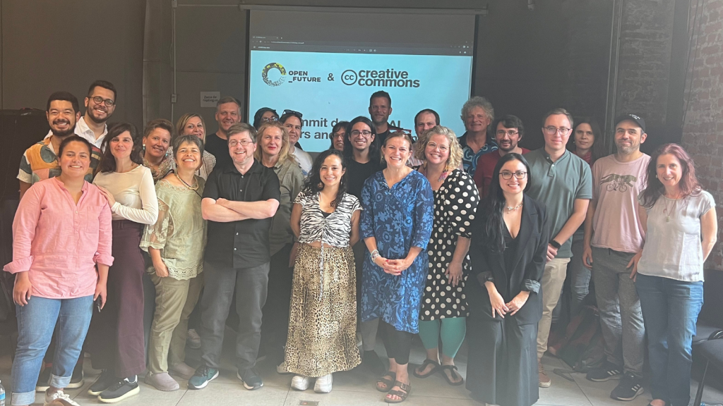 A group of about 20 people standing in a room with a slide behind them that says Open Future & Creative Commons.